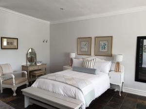 a white bedroom with a bed and a chair at Military House in Pietermaritzburg