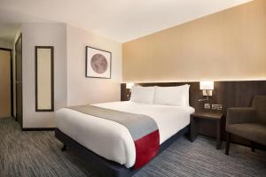 a hotel room with a bed, chair, and nightstand at Ramada Bristol West in Easton in Gordano
