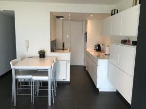 una cocina con armarios blancos y una mesa y sillas blancas. en Marjolaine Zeezicht - Nieuwpoort-bad met GRATIS garagebox en Nieuwpoort