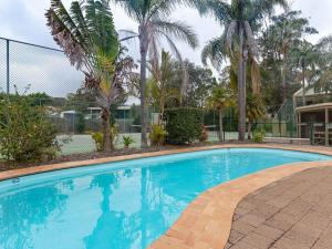 a large swimming pool with palm trees and a fence at Carindale, 2 19-23 Dowling Street - First floor unit with air con, complex pool and tennis court in Nelson Bay