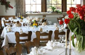 un comedor con mesas y sillas blancas y flores rojas en Landgasthof Sonne, en Mainhardt