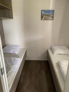 2 letti in una camera con pareti bianche e pavimenti in legno di Luxe Chalet dichtbij Zoutelande a Biggekerke