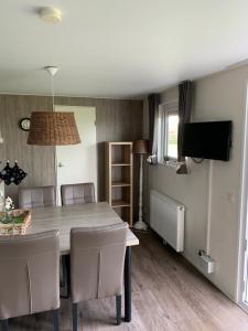 ein Esszimmer mit einem Tisch, Stühlen und einem TV in der Unterkunft Luxe Chalet dichtbij Zoutelande in Biggekerke