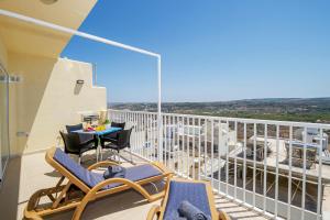 uma varanda com cadeiras e uma mesa num edifício em Summer Breeze apartment with terrace with Panoramic views - by Getawaysmalta em Mellieħa