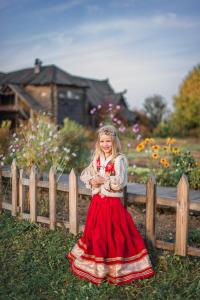 una niña con un vestido rojo de pie junto a una valla en HOT SPRINGS, en Suzdal