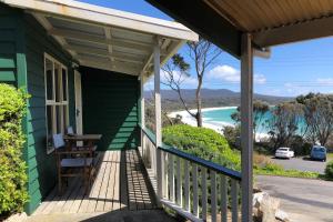 a green house with a porch with a view of the beach at BINALONG BEACH COTTAGE Beachfront at Bay of Fires Next to Restaurant in Binalong Bay