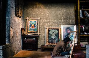 Arro Khampa By Zinc Journey Shangri-la في شانغريلا: شخص يجلس على كرسي في غرفة بها لوحات