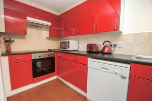 a red kitchen with white appliances and red cabinets at Brighton Townhouse - Central- by Brighton Holiday Lets in Brighton & Hove