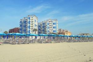 a beach with chairs and blue umbrellas and buildings at Nettuno 9C in Lido di Pomposa