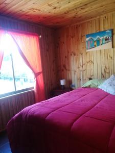 a bedroom with a bed with a purple blanket and a window at Cabañas Tu Bosque in Isla Negra