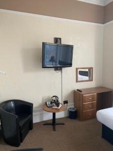 Habitación de hotel con silla, escritorio y TV. en Onslow bed and breakfast, en Glasgow