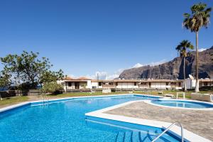 a swimming pool with palm trees and mountains in the background at GIGANTES Oasis Deluxe by Sunkeyrents in Santiago del Teide