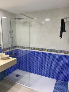 bagno con doccia in vetro e piastrelle blu di Oasis Fuerteventura Beach Apartments a Corralejo