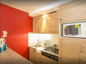 a kitchen with red walls and a sink and a microwave at Residence Le Christiana - maeva Home in La Tania