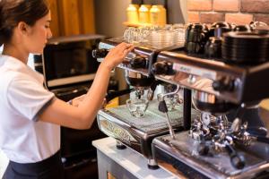 a woman is making a glass in a espresso machine at Aurico Kata Resort & Spa - SHA Extra Plus in Kata Beach