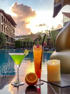 two cocktails and a candle on a table next to a pool at Aurico Kata Resort & Spa - SHA Extra Plus in Kata Beach