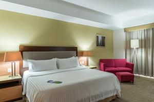 ein Hotelzimmer mit einem Bett und einem roten Stuhl in der Unterkunft Holiday Inn Guadalajara Select, an IHG Hotel in Guadalajara