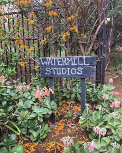 a sign in front of a garden with flowers at Watermill Studios in Gordonʼs Bay