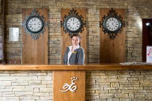 a woman standing behind a counter with clocks on the wall at SPA Hotel Elbrus in Velingrad