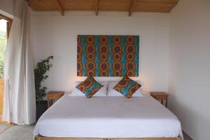 a bedroom with a white bed with a painting on the wall at La Fora Ecolodge in São Filipe