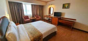 een hotelkamer met een bed, een bureau en een televisie bij Margherita Plaza Hotel in Bintulu