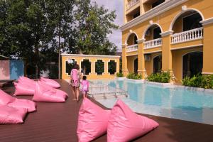a woman and a child walking by a pool with pink pillows at The Pineapple Hotel in Krabi