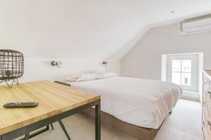 a white bedroom with a bed and a wooden table at Brit Hotel Bristol Montbéliard Centre in Montbéliard