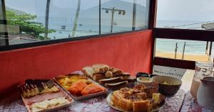 a table topped with different types of bread and pastries at Suítes Pouso do Sol in Praia de Araçatiba