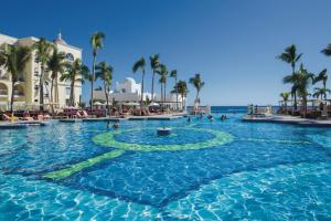 a swimming pool at a resort with palm trees and the ocean at Riu Palace Cabo San Lucas - All Inclusive in Cabo San Lucas