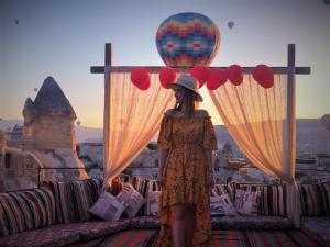 a woman standing on a balcony with a hot air balloon at Antique Terrace Cave Suites in Goreme