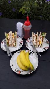 three plates of sandwiches and bananas on a table at The House at Pranburi in Pran Buri