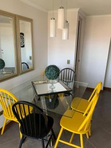 a dining room with a glass table and yellow chairs at MATI´S APARTAMENT in Antofagasta