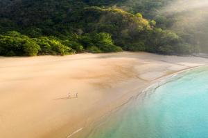 two people standing on a beach next to the water at Six Senses Con Dao - Turtle Island Paradise in Con Dao