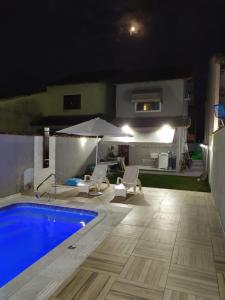 a swimming pool at night with a table and an umbrella at Casa do sagú in Maricá