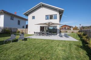 a white house with a patio with chairs and an umbrella at Design Ferienhaus 195qm in Breitbrunn am Chiemsee
