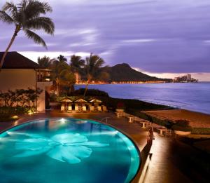 a swimming pool with a view of the ocean at night at Halekulani in Honolulu