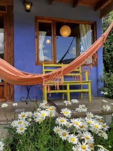 a hammock in front of a blue house with flowers at Cabañas Las Nativas in Lago Puelo