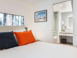 een slaapkamer met een wit bed en een oranje kussen bij Novotel Deauville Plage in Deauville