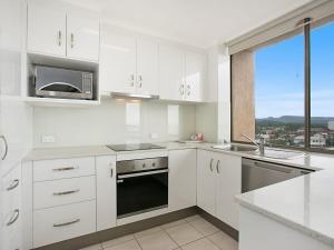 una cucina con armadi bianchi, lavandino e finestra di Kirra Gardens Unit 30 a Gold Coast