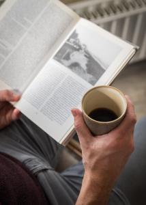 een persoon die een boek en een kopje koffie leest bij Prominent Inn Hotel in Noordwijk aan Zee