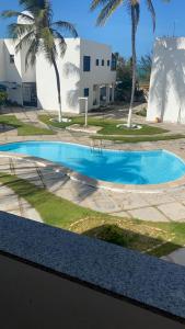 a swimming pool with palm trees in front of a building at Porto Canoa Apartamento in Aracati
