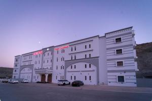 een groot wit gebouw met auto's geparkeerd op een parkeerplaats bij Riyam Hotel in Muscat