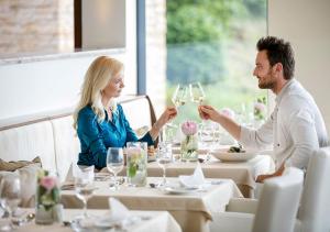 un hombre y una mujer sentados en una mesa con copas de vino en Quellenhotel Heiltherme Bad Waltersdorf - 2-Thermenresort en Bad Waltersdorf