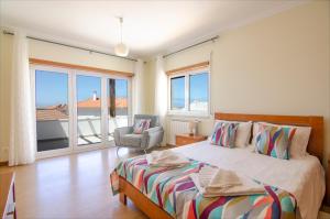 Un dormitorio con una cama y una silla y ventanas. en Baleal Sunset Residence, en Baleal
