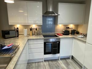 a kitchen with white cabinets and a black microwave at Marie’s Serviced Apartment 1 Bed CityStay, parking in Bedford