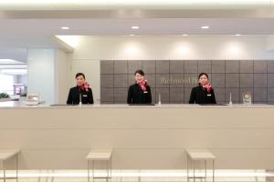 three people wearing bow ties standing behind a counter at Richmond Hotel Fukuyama Ekimae in Fukuyama