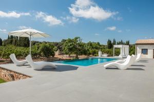 a swimming pool with white chairs and an umbrella at Villa Son Calet 156 by Mallorca Charme in Llubí