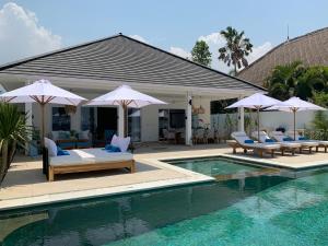 una piscina con sillas y sombrillas junto a una casa en Beachfront Rice Field View Lovina Villa Serenity Bali, en Pengastulan