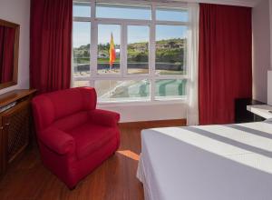 a bedroom with a red chair and a window at Hotel Sablón in Llanes