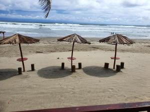 Tres sombrillas en una playa con el océano en Bungalows La Perla Playa Azul, en Playa Azul